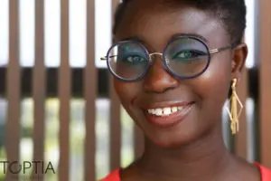 Close-up portrait of a smiling woman with glasses and gold earrings, radiating warmth and confidence. Photo by Tia Haygood.