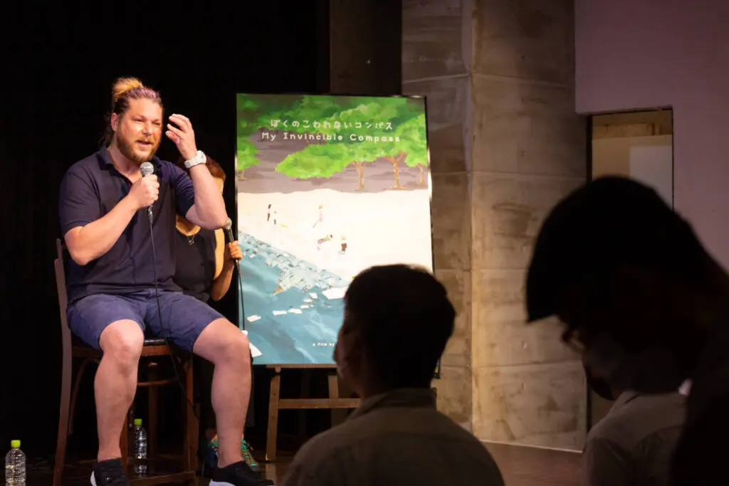 A man in a shirt and a short on the stage talking with the people at the Symposium of a movie - Tokyo Portrait Photographer