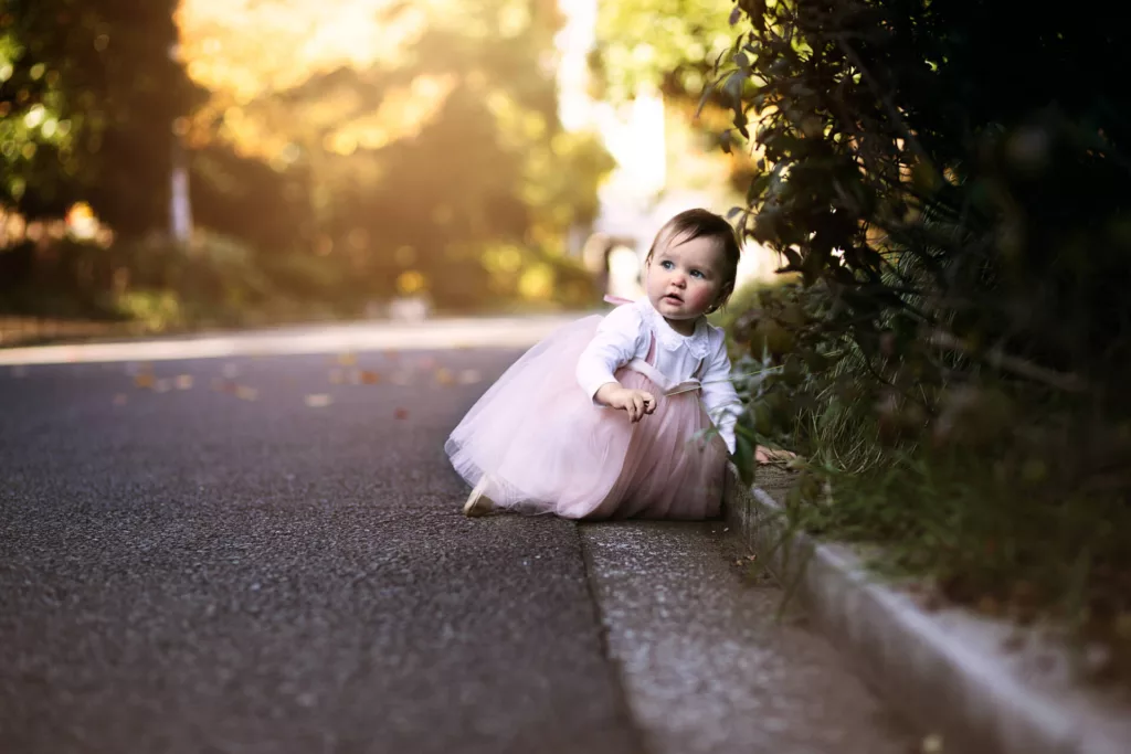 A cute baby girl in a pink dress sitting in a limping position outdoors - family photography, lifestyle photography