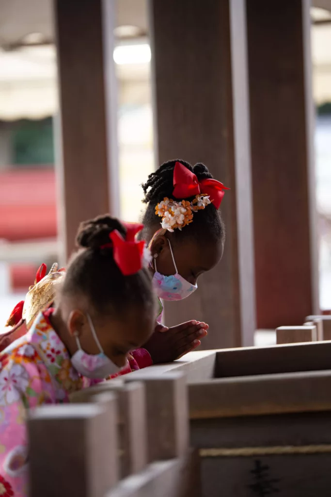 Two little twin girls with same outfits praying by bowing down at a shrine - family photography, lifestyle photography