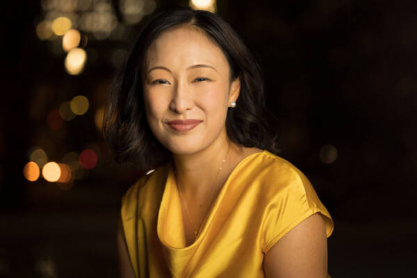 A headshot photo of a beautiful woman in a yellow dress, smiling at the camera. Taken by a portrait photographer in Charlotte