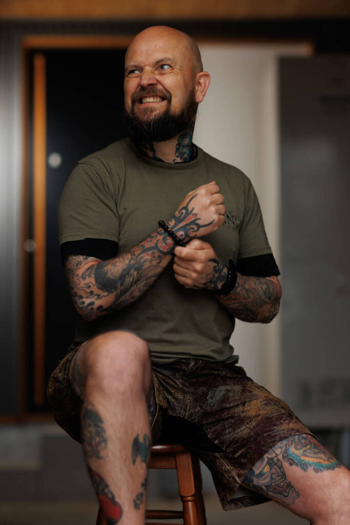 A bald man with several tattoos, sitting indoors with a unique smile - Tokyo Portrait Photographer, Headshot photos