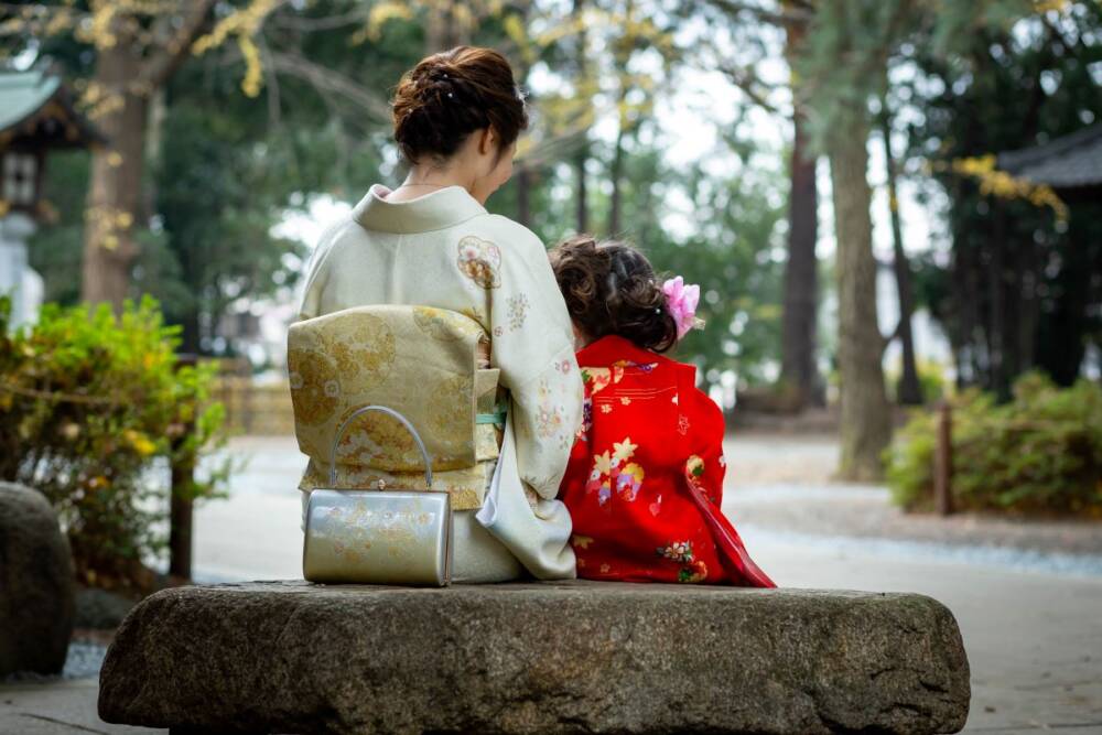 A portrait taken from the back of a mother and a daughter sitting on a big stone roadside - family photography