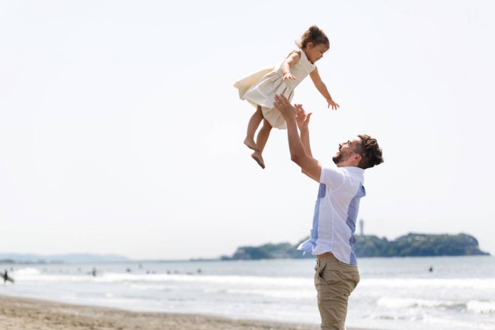 A father raising his little daughter high in the air joyfully on the beach - family photography, lifestyle, Japan Photography