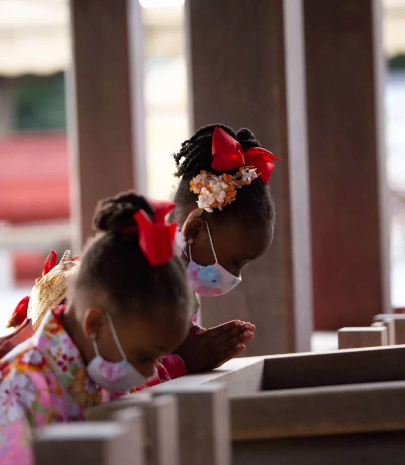 Two little twin girls with same outfits praying by bowing down at a shrine - family photography, lifestyle photography